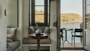 A room with a view of a lake and hills, a window with a view, a table with a vase, and a bench with cushions.