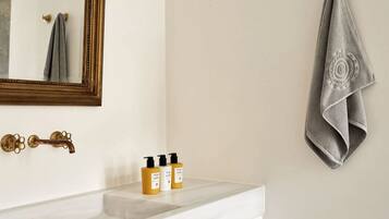 A bathroom with a white sink, a mirror with a gold frame, a towel hanging on the wall, and three bottles of toiletries on the counter.