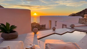 Una terraza en la azotea tranquila con vistas al atardecer, que cuenta con una piscina, sillones de descanso y una planta en maceta.