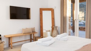 Un dormitorio con cama, un banco de madera, televisor, espejo y vistas al exterior.