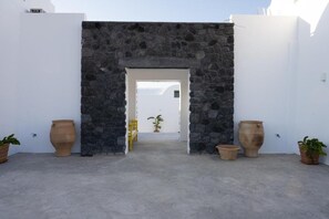 A stone archway leading to a doorway, flanked by white walls and potted plants. - Exquisite Santorini Villa | Villa Metis | 2 Bedrooms | Private Pool | Beautiful. (Oia)
