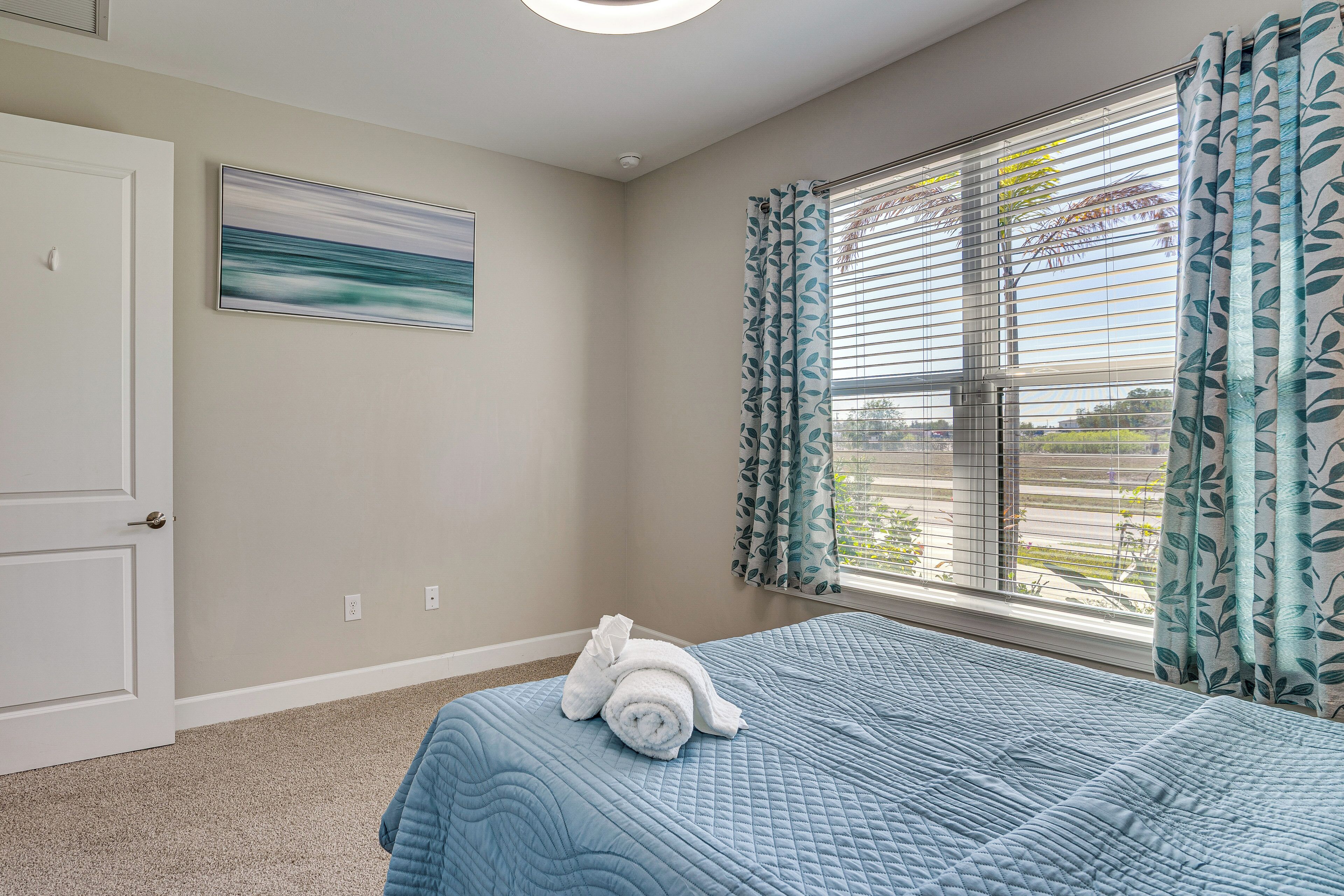 A bedroom with a bed, a window with curtains, a door, and a painting on the wall.
