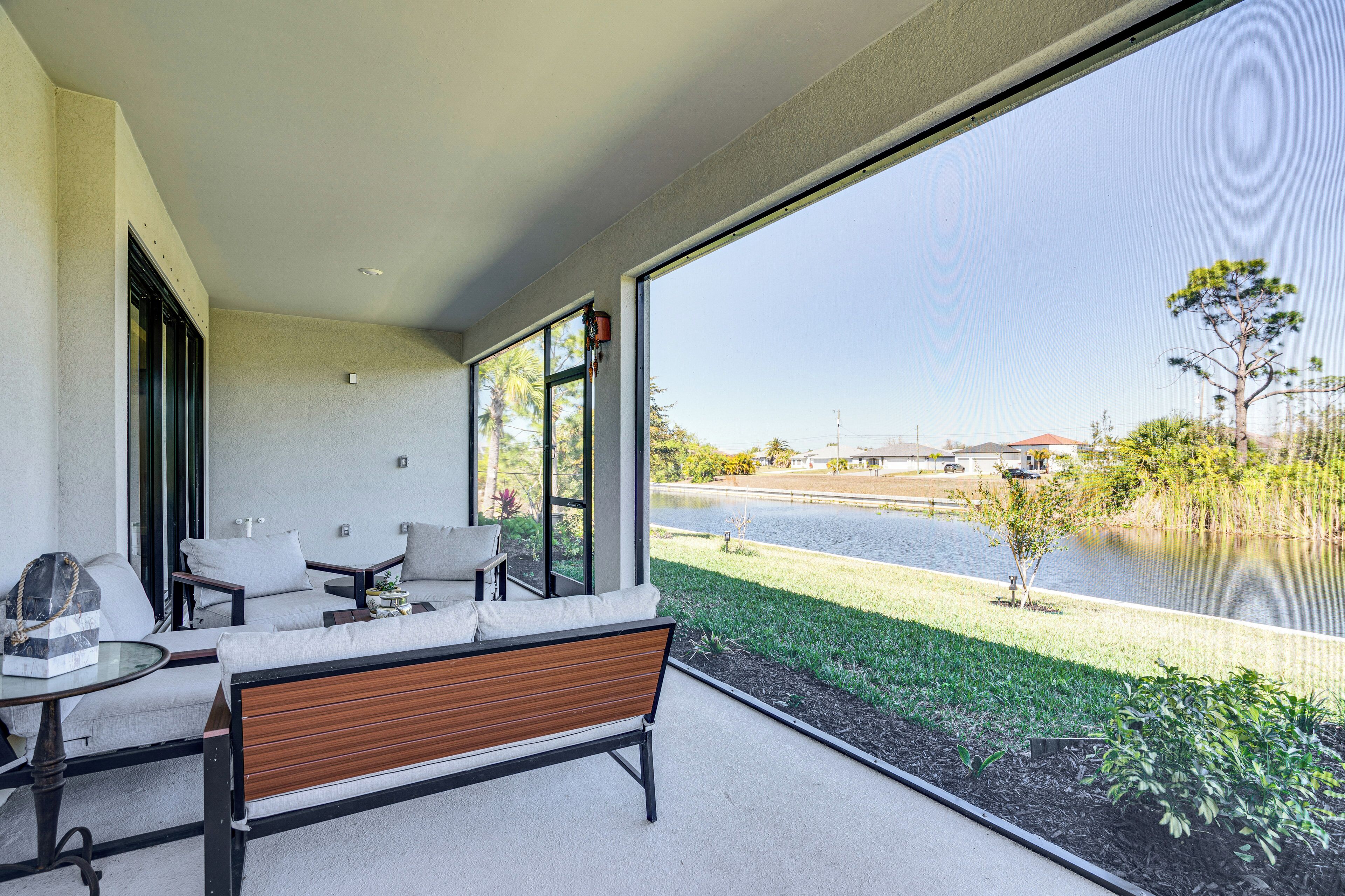 A modern outdoor seating area with a bench and chairs, overlooking a body of water and a park.