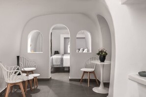 A modern hotel room with white furniture, a small round table, and a potted plant. - Magnificent Santorini Room | Aegean Serenity Room | Breathtaking Caldera and. (Oia)