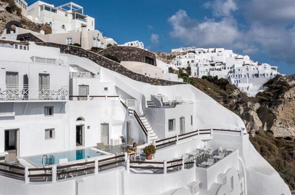 Um edifício branco com piscina e área de estar ao ar livre, rodeado por outros edifícios brancos numa encosta.