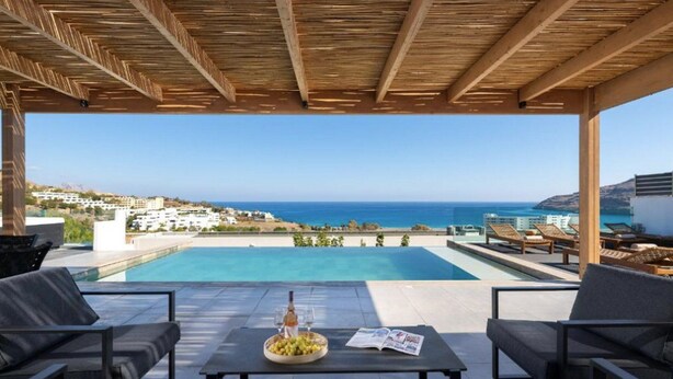 Zona junto a la piscina con vista al mar, mobiliario exterior y una mesa con botella y vasos.