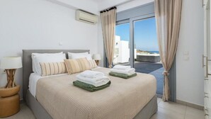 Habitación de hotel con cama, mesita de noche, lámpara y vista al mar a través de las puertas del balcón.