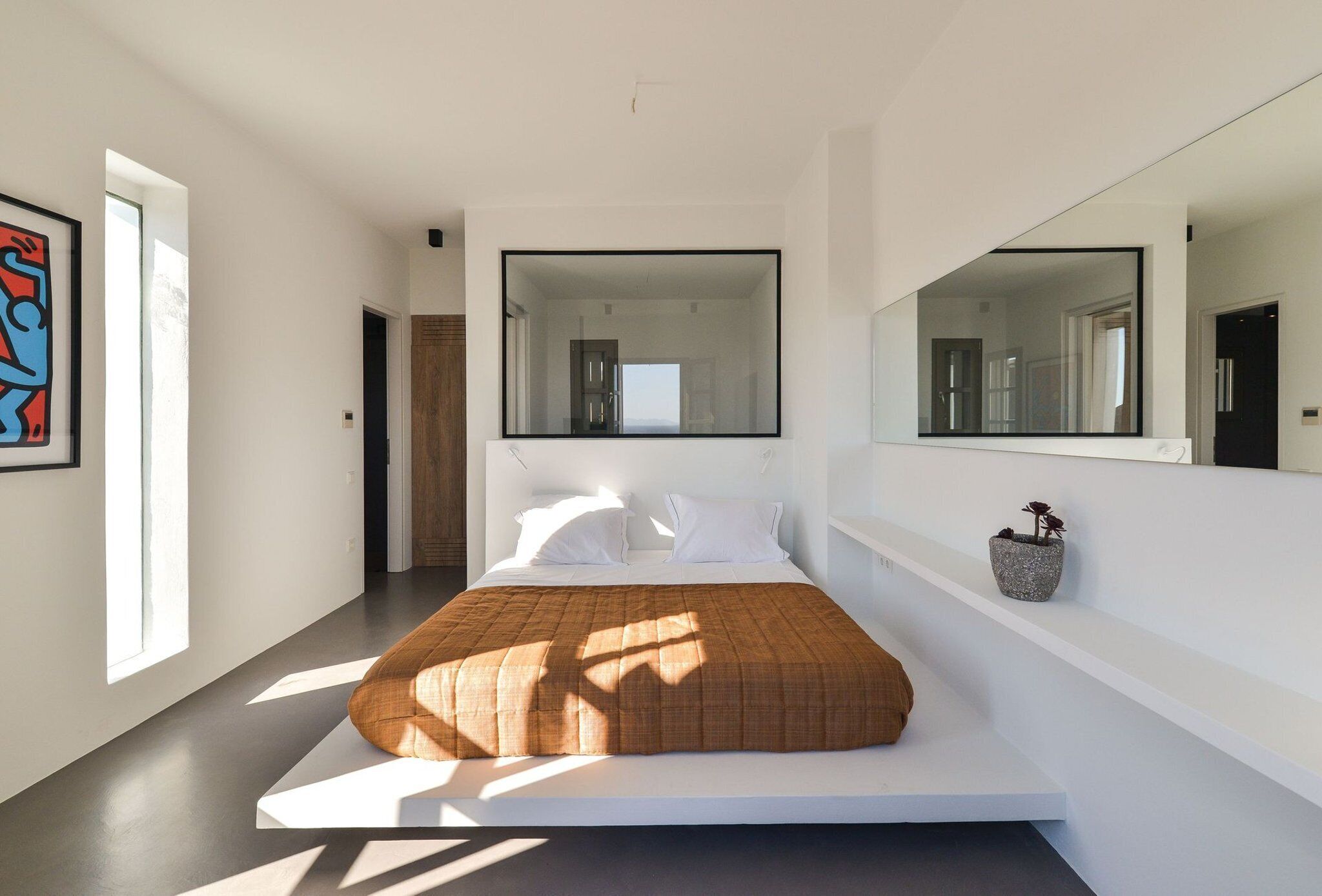 A modern bedroom with a bed, large windows, and a wall-mounted mirror.