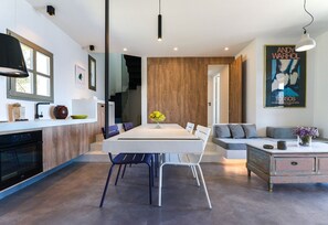 A modern kitchen with a dining area, wooden accents, and a poster of Andy Warhol's 'Torsos'. - Superb Tinos See Front Villa | Villa Themis | 1 Bedroom | Breathtaking Sea. (Tinos)
