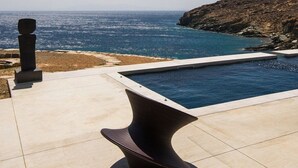 A modern outdoor pool area with a view of the ocean and a rocky coastline.
