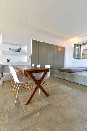 Un comedor moderno con una mesa de madera y sillas blancas, un banco empotrado y un suelo de baldosas de piedra.