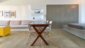 Ein modernes Wohnzimmer mit Esstisch, weißen Stühlen, einer Couch und einem gelben Beistelltisch.