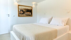 A minimalist bedroom with a large bed, a painting of a car on the wall, and a door to the left.