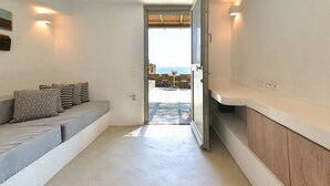 A modern interior with a built-in bench, a doorway leading to an outdoor area with a table and chairs, and a view of the sea.