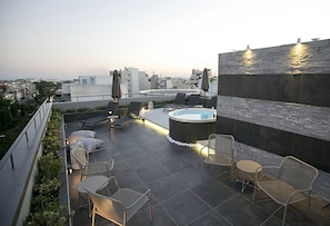 A rooftop terrace with a hot tub, lounge chairs, and umbrellas.