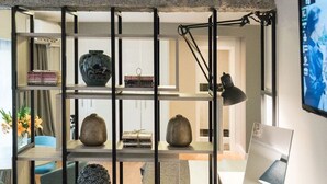 A modern office space with a desk, chair, and shelving unit containing books and decorative items. - Lavish Athens Loft | Zephyr Loft | 1 Bedroom | Superb City Views | Prime. (Athens)