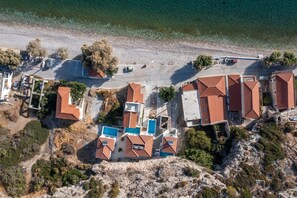 An aerial view of a coastal resort with multiple buildings, a swimming pool, and a beach.