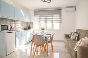 A modern kitchen with light blue cabinets, a dining area with a table set for four, and a beige sofa with decorative pillows.