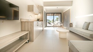 Una sala moderna con una televisión de pantalla plana, un sofá, una mesa de comedor y una zona de cocina con un fregadero y armarios.