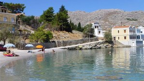 A coastal area with clear water, a sandy beach, and buildings along the shore. - Superb Symi Villa | Villa Elysian Blue | 4 Bedrooms | Breathtaking Sea Views |. (Symi)