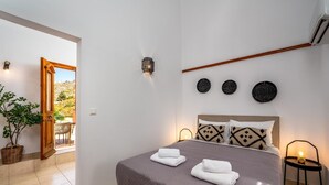 A bedroom with a bed, two wall-mounted lights, a wooden ceiling beam, and three wall-mounted decorative items. - Superb Symi Villa | Villa Elysian Blue | 4 Bedrooms | Breathtaking Sea Views |. (Symi)