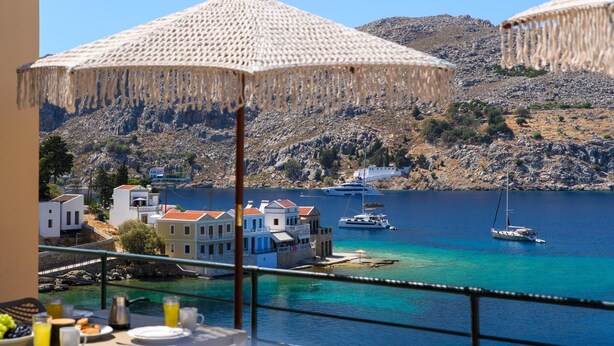 A balcony with a view of a coastal town, a yacht, and a sailboat. - Superb Symi Villa | Villa Elysian Blue | 4 Bedrooms | Breathtaking Sea Views |. (Symi)