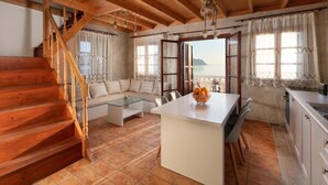 En ombonad inredning med en trätrappa, en soffa, ett soffbord i glas, ett köksområde och utsikt över havet.