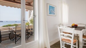 Ein Essbereich mit Tisch und Stühlen, Blick auf das Meer und einem Bild an der Wand.