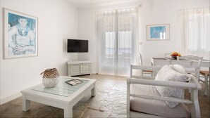 Ein modernes Wohnzimmer mit Flachbildfernseher, einem Glastisch, einem weißen Sofa und einem Essbereich mit Tisch und Stühlen.