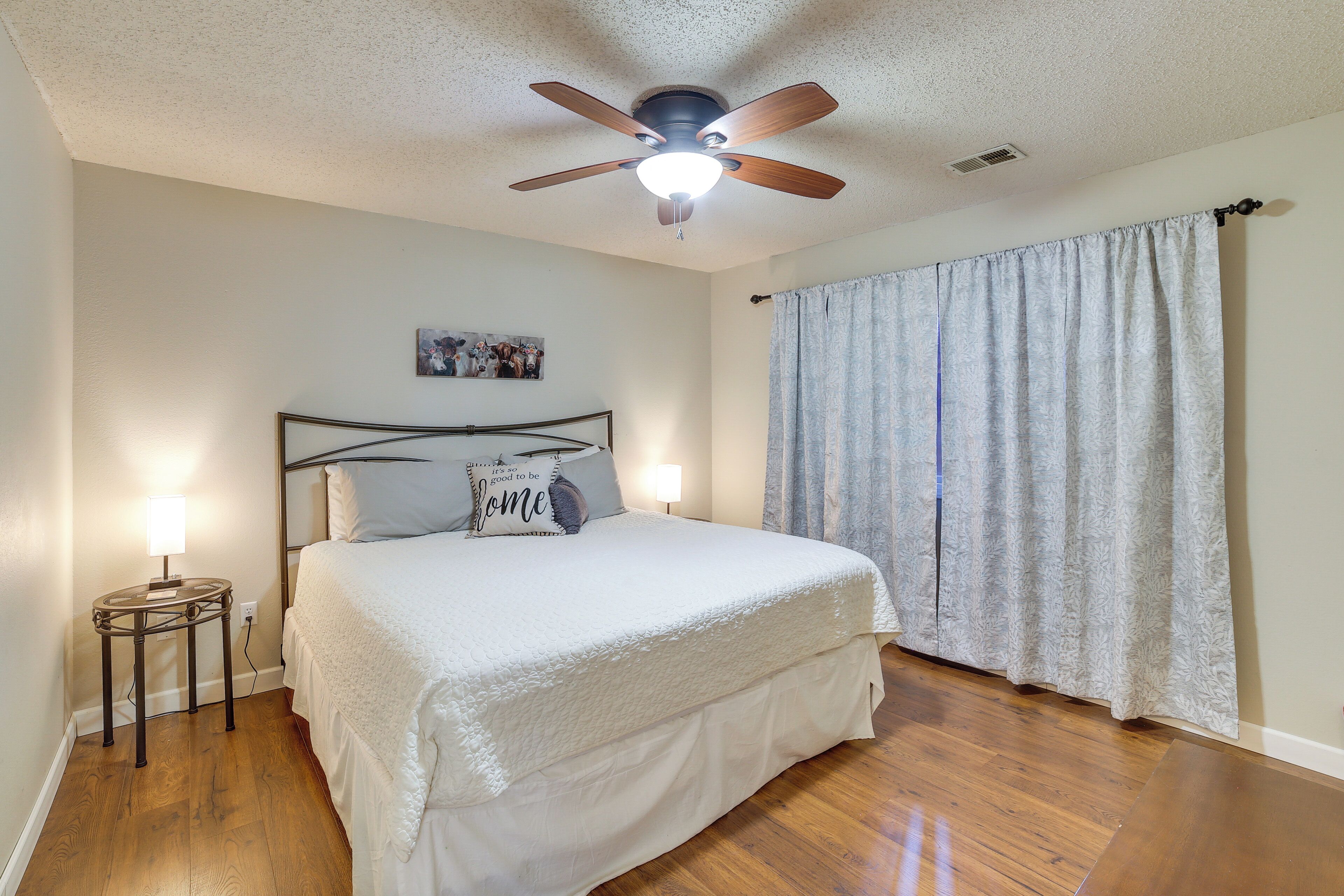 A bedroom with a bed, a ceiling fan, a nightstand, and a window with curtains.