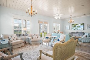 A spacious living room with a high ceiling, large windows, and a variety of seating options including a sofa, chairs, and a rattan chair. - Salty Lashes | Charming Coastal Retreat Near Keira’s Pool and the Lake (Port Aransas)