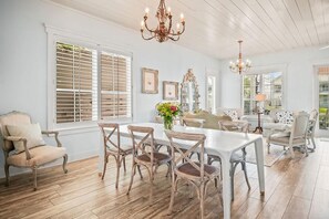 Ein geräumiger Raum mit Esstisch, Stühlen, einer Deckenleuchte und einem großen Fenster mit Jalousien.