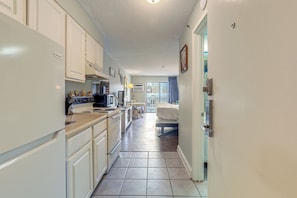 A compact kitchen with white cabinets, a refrigerator, and a dining area with a table and chairs. - Ocean-view Balcony! Couples Escape in Myrtle Beach (Myrtle Beach)