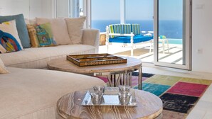 Ein modernes Wohnzimmer mit einer Couch, einem Couchtisch mit Schnapsgläsern und Meerblick durch große Fenster.