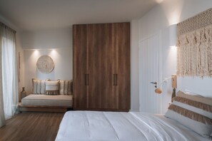 A bedroom with a bed, a sofa, a wooden wardrobe, and a wall-mounted lamp. - Villa Caelith, 2 BDR, Private Pool, Furnished Terrace, Naousa (Paros)