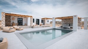 Uma área de piscina moderna ao ar livre, com paredes de pedra, espreguiçadeiras e uma pérgula de madeira.