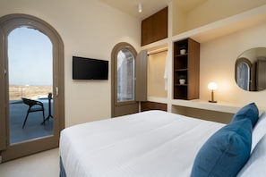 A hotel room with a bed, a TV mounted on the wall, a desk with a chair, and a view of the outside. - Villa Kleonika, 2 BDR, Wonderful Seaviews, Private Pool, Santorini (Santorini)