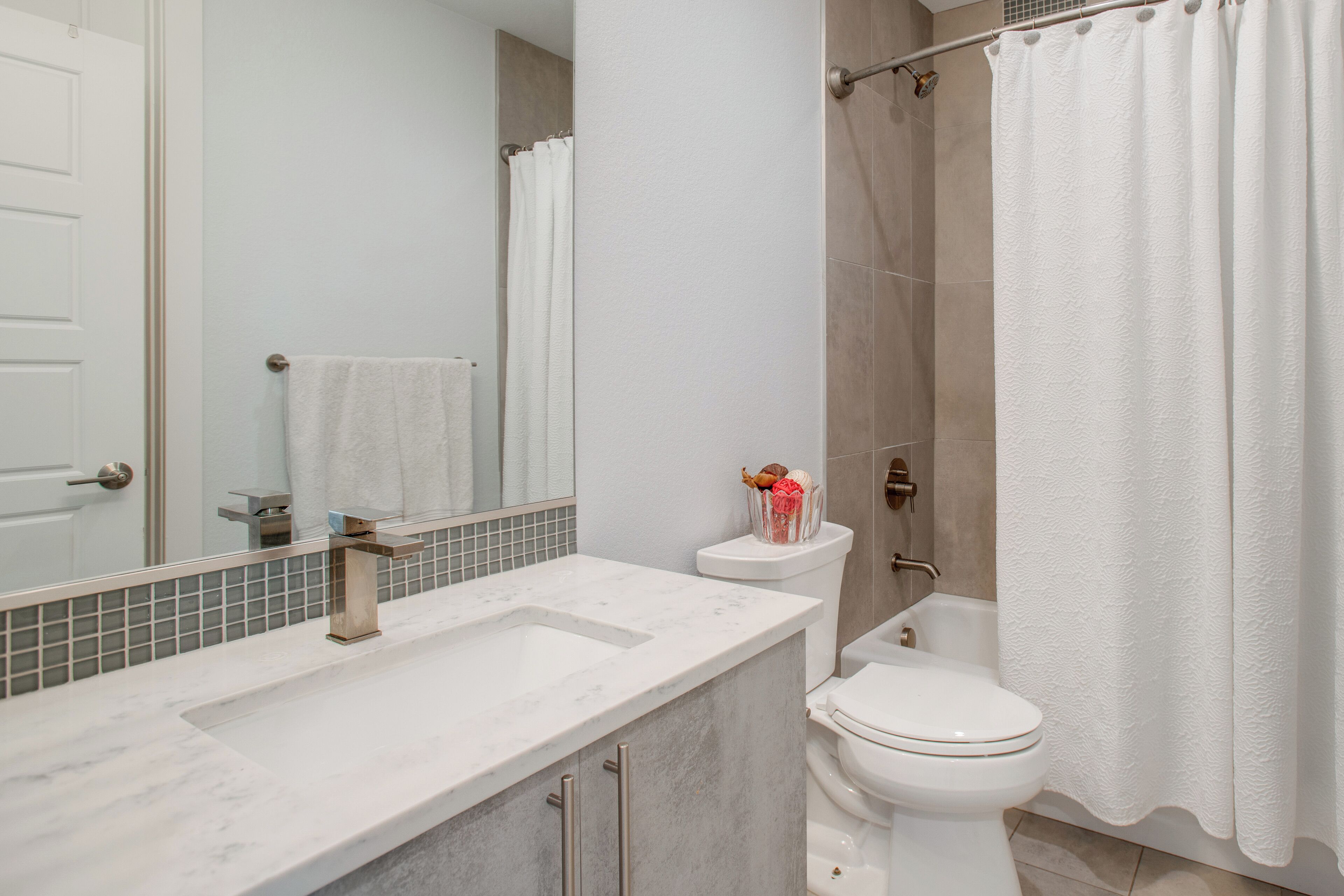 A modern bathroom with a marble sink, a toilet, and a shower curtain.