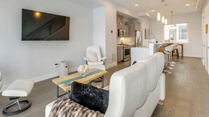 Ein modernes Wohnzimmer mit Flachbildfernseher, einer Couch, einem Couchtisch und einem Essbereich mit Barhocker.