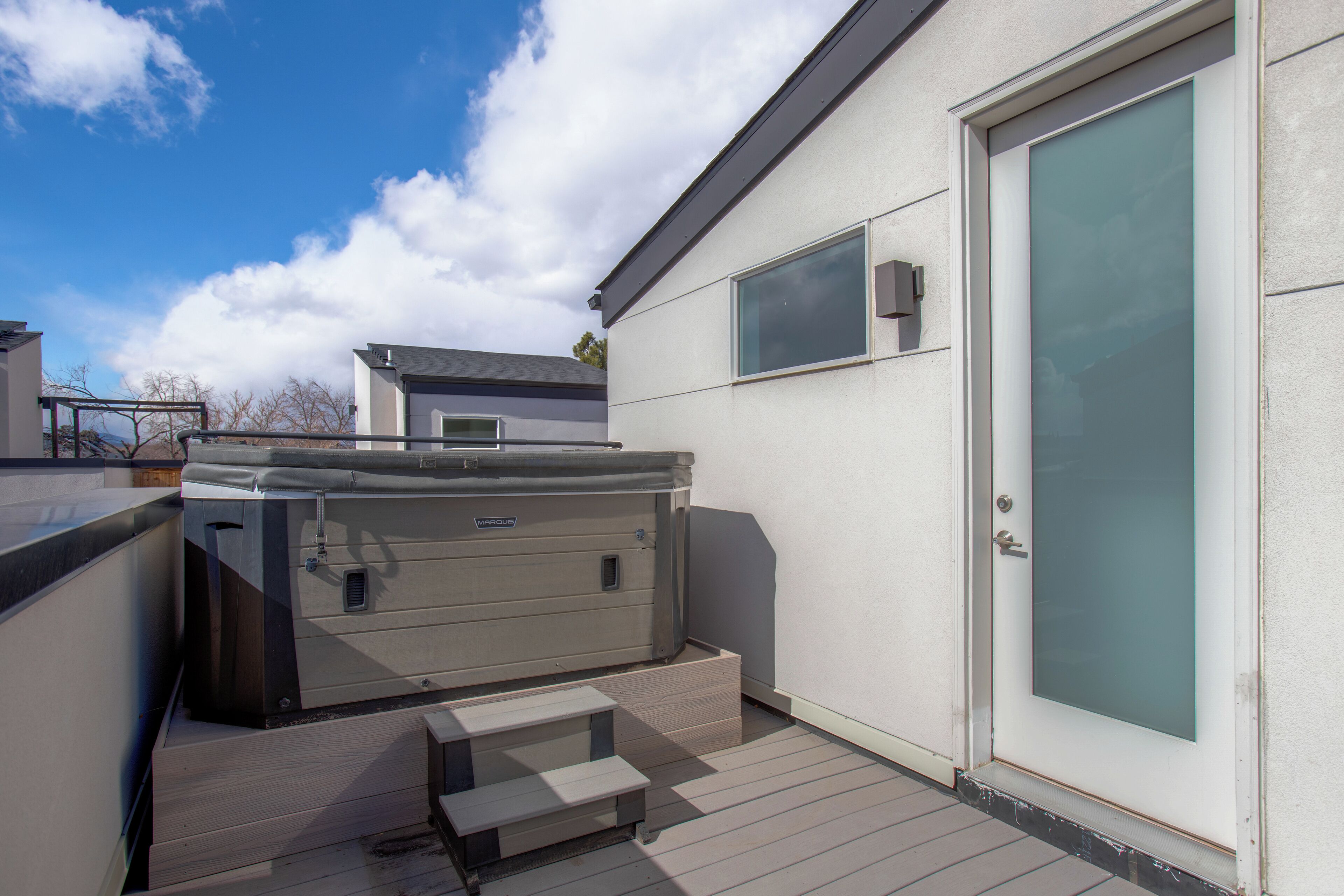 A hot tub on a wooden deck attached to a building with a sliding glass door.
