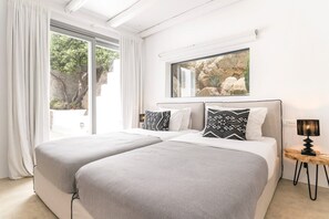 Ein modernes Schlafzimmer mit zwei Betten, einem großen Fenster mit Blick auf Grünflächen und einem kleinen Tisch mit einer Lampe.