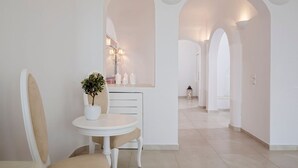 Un couloir aux murs blancs et aux arcades, une table ronde ornée d’une plante en pot et un miroir avec des appliques murales.