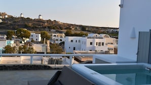 A rooftop terrace with a hot tub, a sofa, and a view of white buildings and a hill with windmills. - Villa Ioneira, Sea Views, Outdoor Hot Tub, Furnished Terrace, Santorini (Santorini)