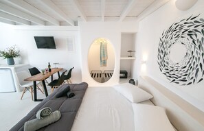 A modern, minimalist room with a sofa, a dining area, and a wall-mounted TV. - Villa Ioneira, Sea Views, Outdoor Hot Tub, Furnished Terrace, Santorini (Santorini)