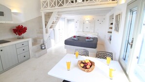 A bedroom with a bed, a dining table with fruit and drinks, a staircase, and a balcony. - Villa Ioneira, Sea Views, Outdoor Hot Tub, Furnished Terrace, Santorini (Santorini)