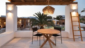 Une terrasse extérieure avec une table ronde en bois et des chaises, un luminaire suspendu et une échelle.
