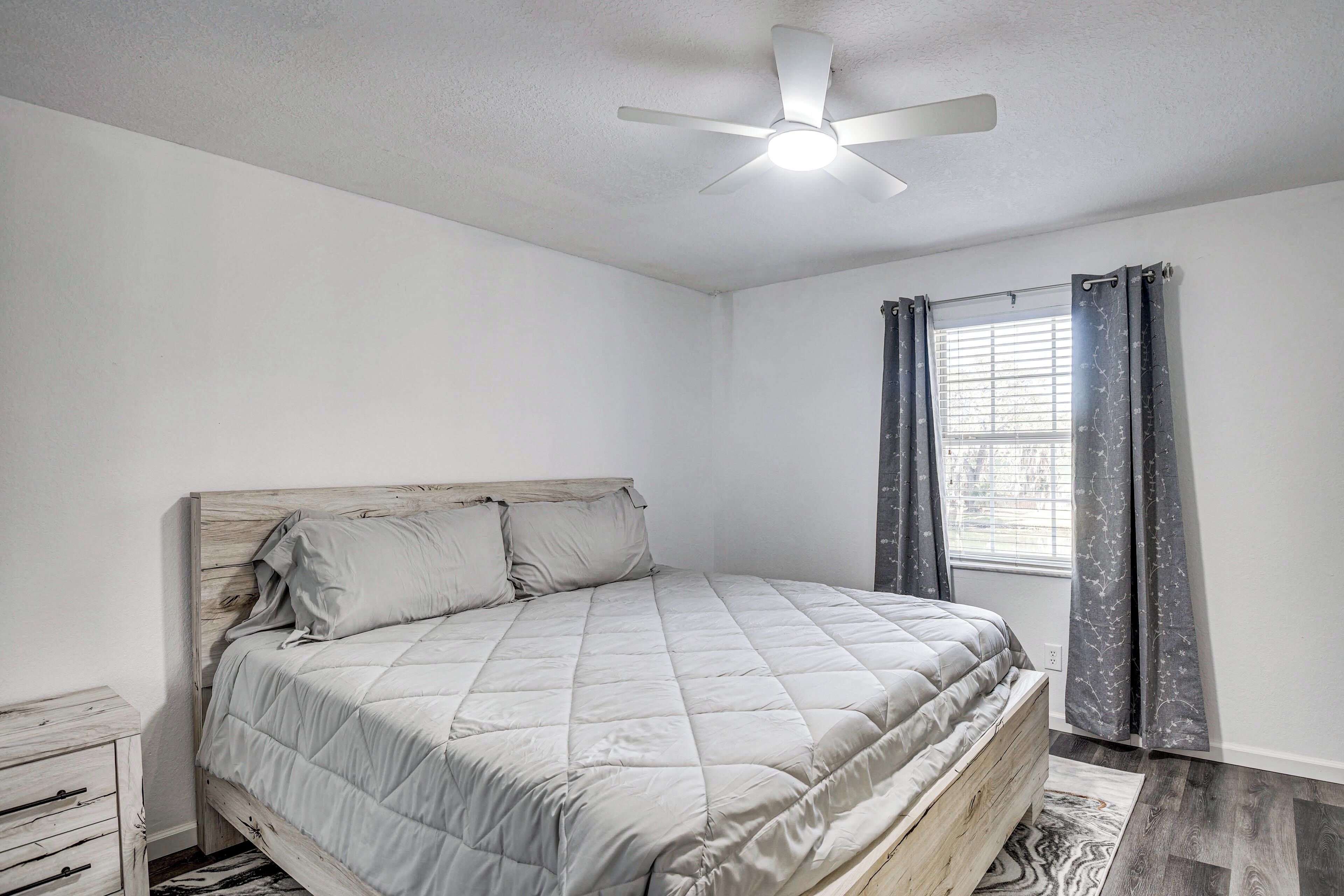 Ein Schlafzimmer mit Bett, Deckenventilator, Fenster mit Vorhängen und Nachttisch.