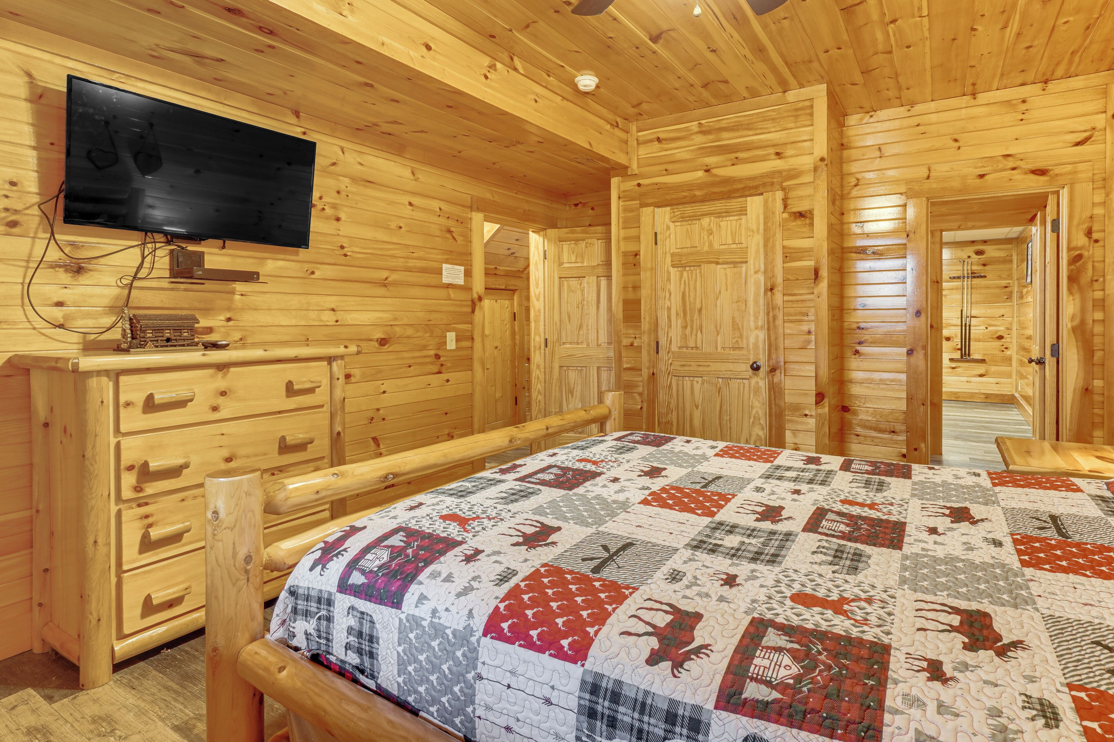 Camera da letto in una baita di legno, con un letto, una cassettiera, un televisore e una coperta con motivi animalier.