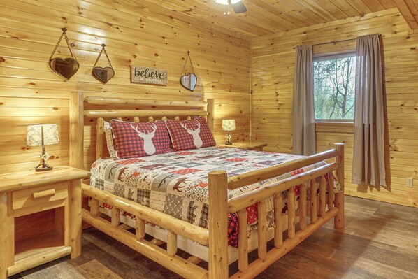A wooden cabin bedroom with a bed, two nightstands, a window with curtains, and a wall with a motivational sign. - Mtn-view Gem w/ Hot Tub + Game Room in Sevierville (Sevierville)