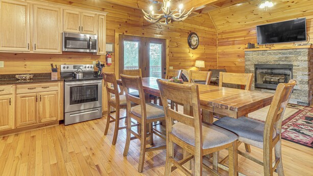 Een houten cabin interieur met een eettafel, stoelen, een open haard, een televisie en keukenapparatuur.